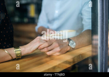 Paar Hand in Hand auf dem Tisch durch das Fenster im Cafe gesehen Stockfoto