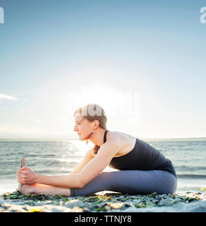 Frau üben sitzt vorn am Strand Biegung gegen den Himmel Stockfoto