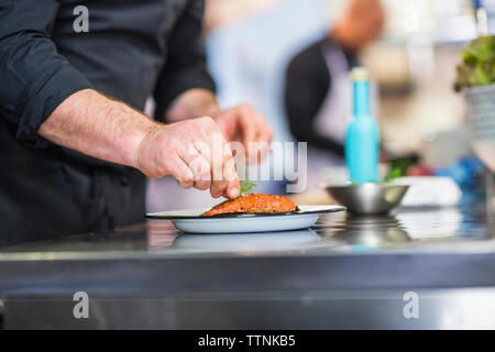 Mittelteil von Chef garnierungen Nahrungsmittel, während Mitarbeiter arbeiten im Hintergrund im Restaurant Stockfoto