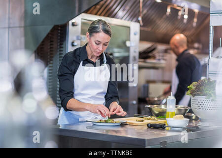 Köchin garnierungen Nahrungsmittel, während Mitarbeiter arbeiten im Hintergrund bei Restaurant Küche Stockfoto
