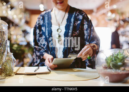 Mittelteil der Eigentümer lesen Kreditkarte über Tablet-PC für die Zahlung in Pflanzen shop Stockfoto