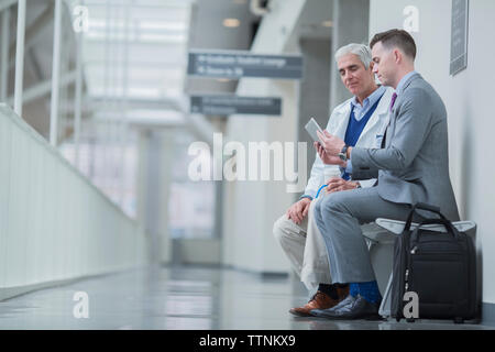 Männliche Ärzte diskutieren über Tablet-PC während auf dem Sitz in Krankenhaus Flur sitzen Stockfoto