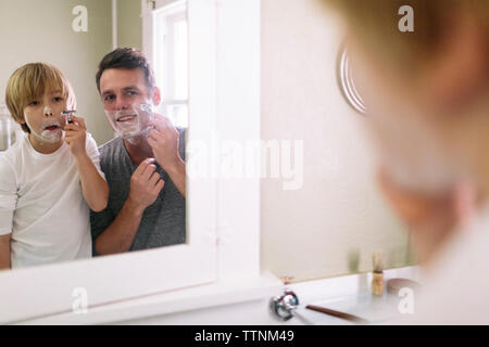 Vater und Sohn während der Rasur in reflektierenden Spiegel Stockfoto