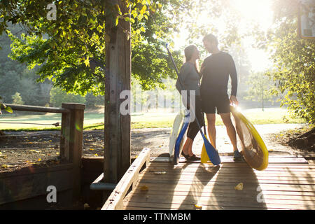 Paar mit paddleboards an einander suchen beim Stehen auf Boardwalk Stockfoto