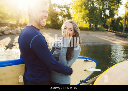 Glückliches Paar mit paddleboards am Flussufer Stockfoto
