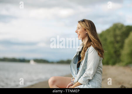 Seitenansicht der glücklichen Frau am Ufer sitzen Stockfoto