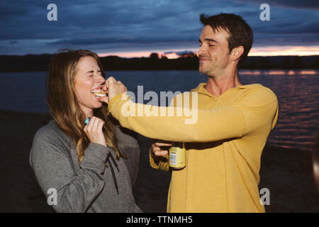 Mann Fütterung smore auf weibliche Freunde gegen River bei Sonnenuntergang Stockfoto