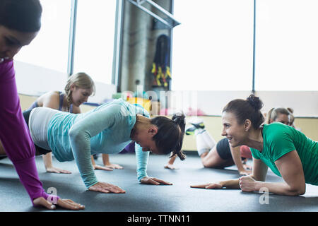 Kursleiter motivierender Frau dabei Push-ups im Fitnessstudio Stockfoto