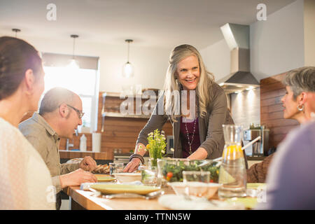 Frau das Essen für Freunde am Esstisch sitzen Stockfoto