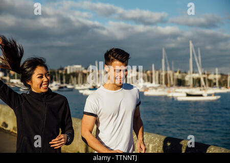 Glückliches junges paar Joggen während des Trainings an der Promenade gegen bewölkten Himmel in der Stadt Stockfoto