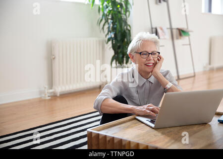 Senior Geschäftsfrau mit Laptop während der Sitzung auf dem Teppich im Büro Stockfoto