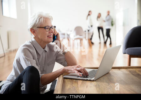 Senior Geschäftsfrau Gespräch am Handy mit Laptop Stockfoto