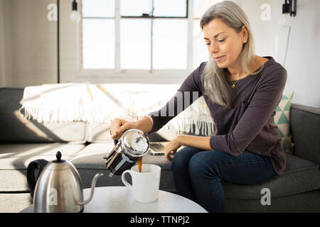 Frau gießen Kaffee in der Tasse auf dem Tisch zu Hause Stockfoto