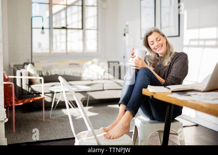Nachdenkliche Frau mit Kaffeetasse sitzend auf Stuhl Stockfoto