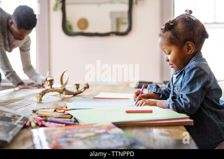 Seitliche Sicht auf Mädchen Färbung in Buch mit Vater im Hintergrund zu Hause Stockfoto