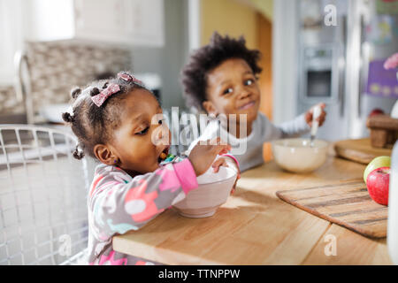 Mädchen essen Frühstück Getreide während Bruder bei ihr in der Küche auf der Suche Stockfoto