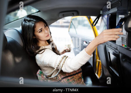 Junge Frau, die kontaktlose Zahlung durch Smart Phone im Taxi Stockfoto