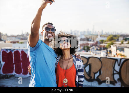 Paar in Sonnenbrille unter selfie gegen Himmel am Gebäude Terrasse Stockfoto