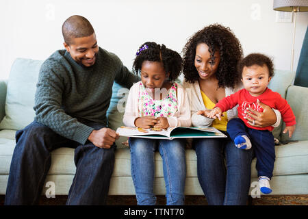 Happy Family suchen in Bild Buch beim Sitzen auf dem Sofa Stockfoto