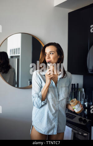 Frau lecken Löffel, während in der Küche stehend Stockfoto