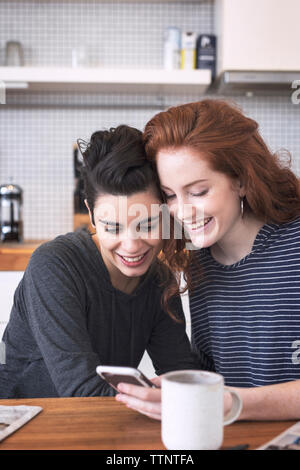 Gerne Lesben mit Handy während durch Esstisch zu Hause sitzen Stockfoto