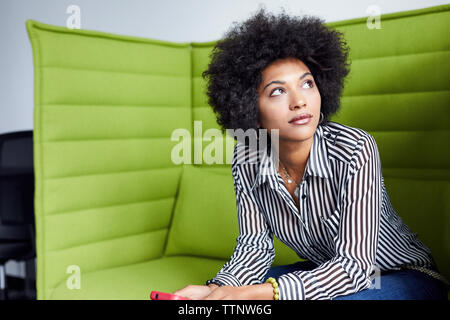 Geschäftsfrau, die wegschaut, während sie im Büro auf dem Sofa sitzt Stockfoto