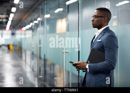Nachdenklich Geschäftsmann Holding smart phone beim Stehen in der Lobby im Büro Stockfoto