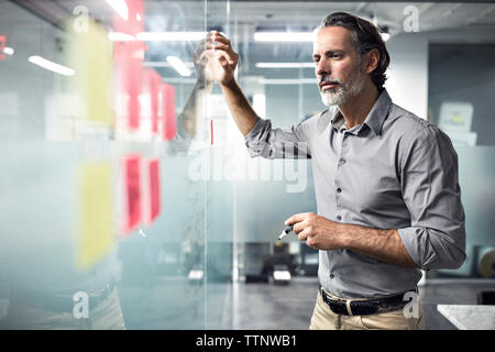 Geschäftsmann, der sich Haftnotizen am Fenster im Büro ansieht Stockfoto