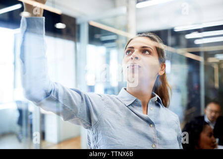 Nahaufnahme der jungen Geschäftsfrau schreiben auf Glas im Büro Stockfoto