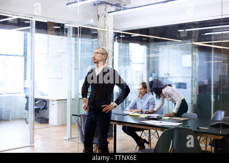 Zuversichtlich Unternehmer stehen mit Hand auf der Hüfte, während die weiblichen Kollegen diskutieren Konferenztisch Stockfoto