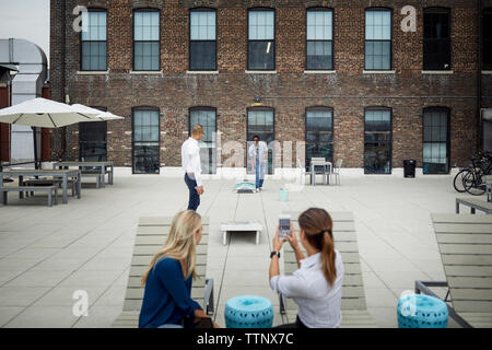 Geschäftsfrau fotografiert Geschäftsmann, der auf der Terrasse spielt Stockfoto