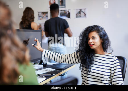 Weiblichen Kollegen am Tisch, während Geschäftsleute an Foto Ausdrucke auf Bulletin Board im Büro Stockfoto
