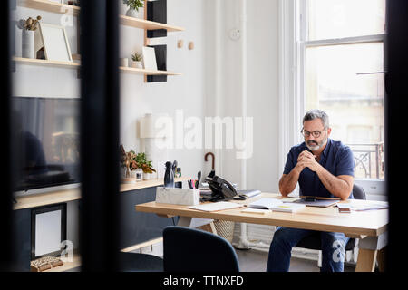 Nachdenklich Geschäftsmann am Schreibtisch in Creative office durch das Fenster gesehen sitzen Stockfoto