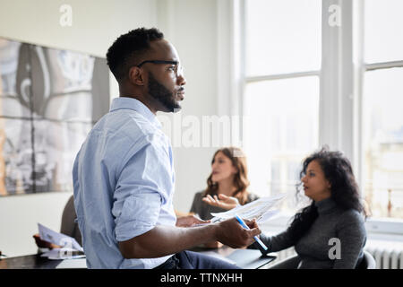 Nachdenklich Geschäftsmann holding Dokumente, während die weiblichen Kollegen diskutieren kreative Büro Stockfoto