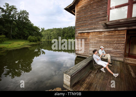 Senior paar Sitzen auf Stühlen, die durch hölzerne Haus am See Stockfoto
