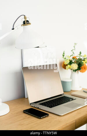 Hohe Betrachtungswinkel und der Technologien mit Leselampe und Blumenvase auf hölzernen Tisch gegen die Wand im Büro Stockfoto