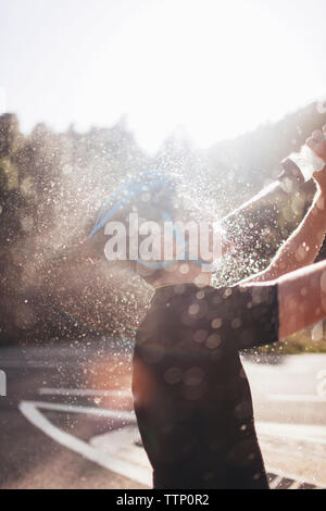 Seitenansicht der Radfahrer spritzen Wasser auf Gesicht in sonnigen Tag Stockfoto