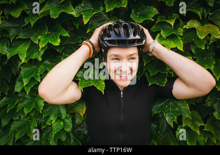 Lächelnd männliche Radfahrer tragen Helm gegen Efeu Stockfoto