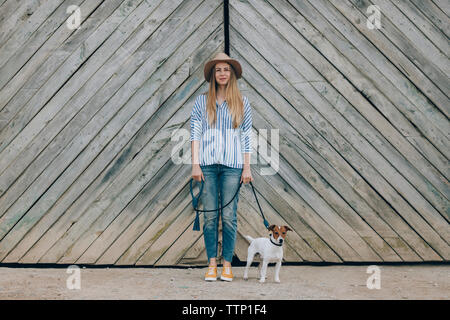 Portrait von Frau mit Jack Russell Terrier stehend gegen hölzerne Tor Stockfoto