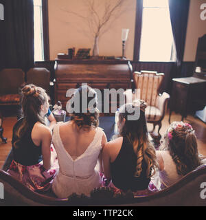 Ansicht der Rückseite des Braut mit Brautjungfern und Flower Girl auf dem Sofa zu Hause sitzen Stockfoto