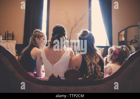 Ansicht der Rückseite des Braut mit Brautjungfern und Flower Girl auf dem Sofa zu Hause sitzen Stockfoto