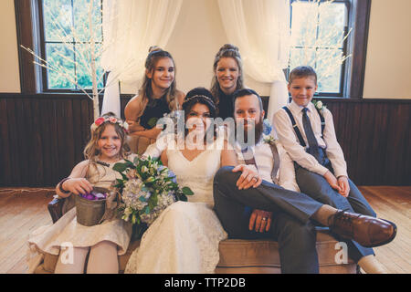 Portrait von jungvermählte Paar von Pageboy und Blumenmädchen mit brautjungfern auf Sofa während der Trauung Stockfoto