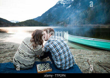 Junges Paar Küssen, beim sitzen auf der Picknickdecke am Seeufer Stockfoto