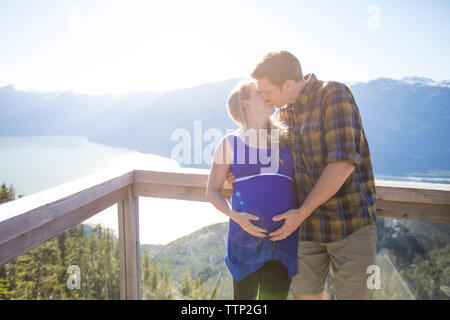 Paar küssen, während sich gegen Berge bei Beobachtung während der sonnigen Tag Stockfoto