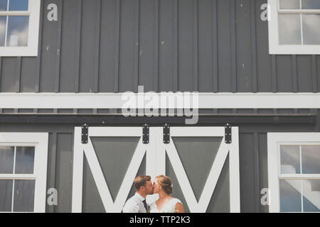 Frisch verheiratete junge Paar küssen gegen Gebäude Stockfoto