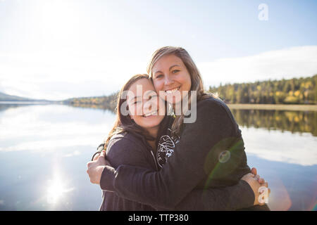 Portrait von fröhlichen weibliche Freunde umarmen gegen See während der sonnigen Tag Stockfoto