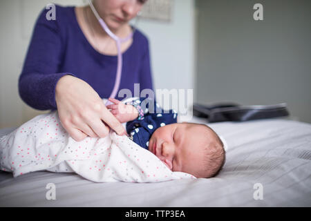 Hebamme Prüfung Neugeborene schlafen Baby Mädchen mit Stethoskop auf Bett zu Hause Stockfoto