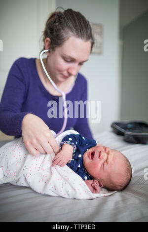 Hebamme Prüfung der neugeborenen Mädchen mit Stethoskop auf Bett zu Hause Stockfoto