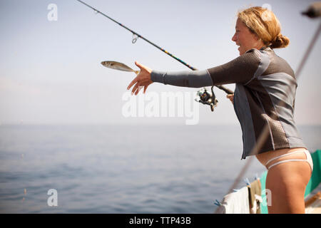 Glückliche Frau loslassen Fisch, während am Ufer stehend Stockfoto