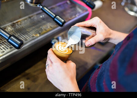 Mittelteil der Barista gießen Milch im Kaffee, während Sie schaumig Getränk im Cafe Stockfoto